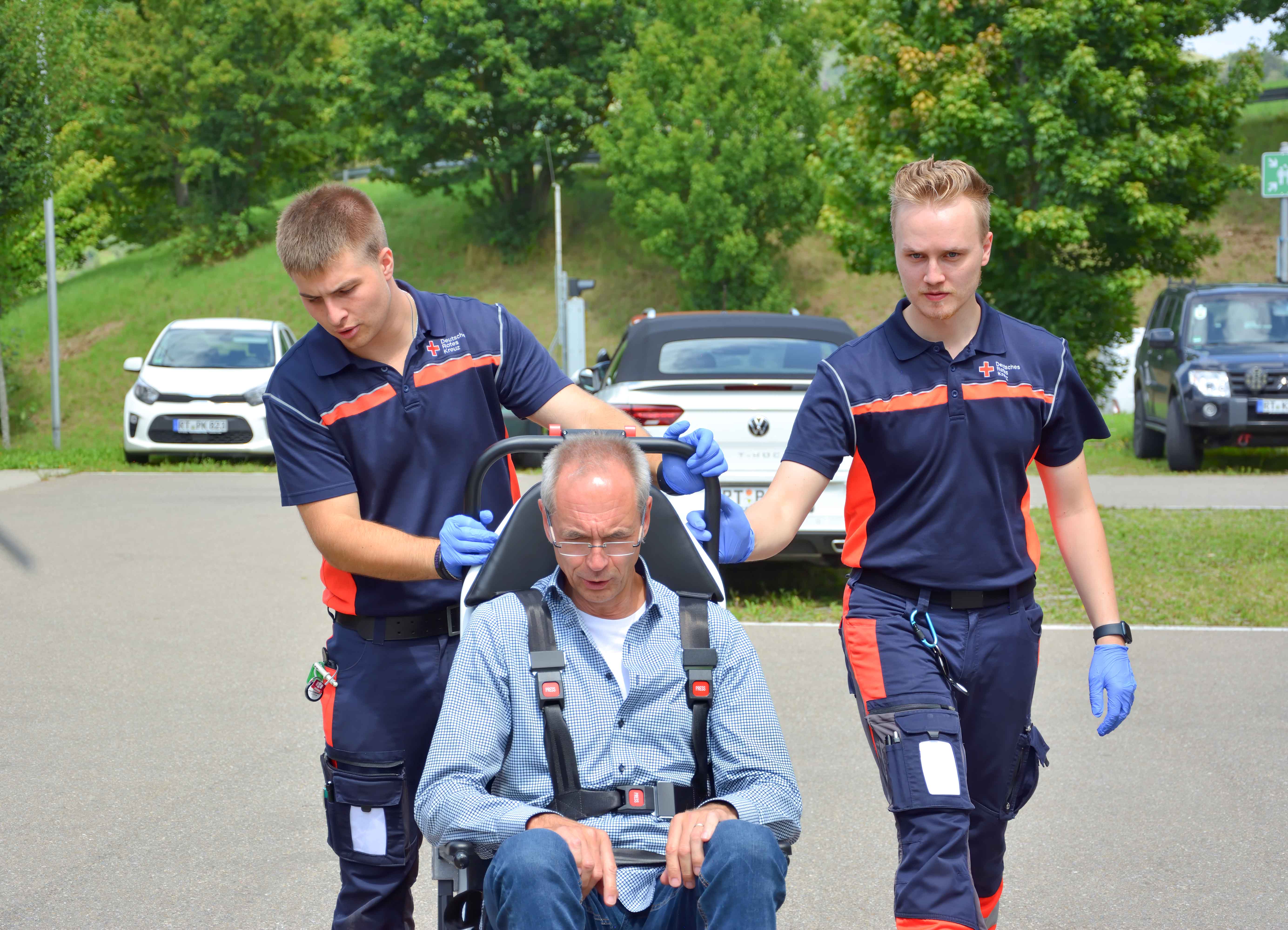 Zum Angebot Krankentransport Zwei Sanitäter versorgen einen Patienten im Transportstuhl