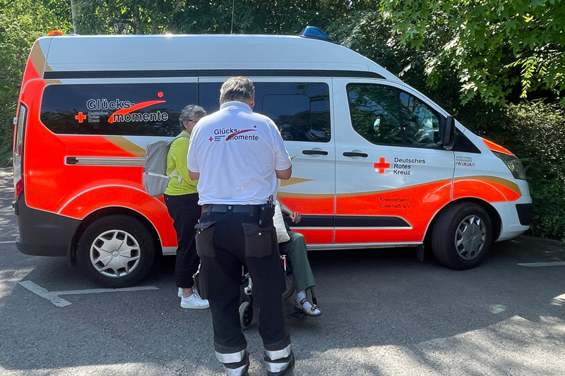 DRK-Mitarbeiter und Rollstuhlfahrer vor einem Krankenwagen