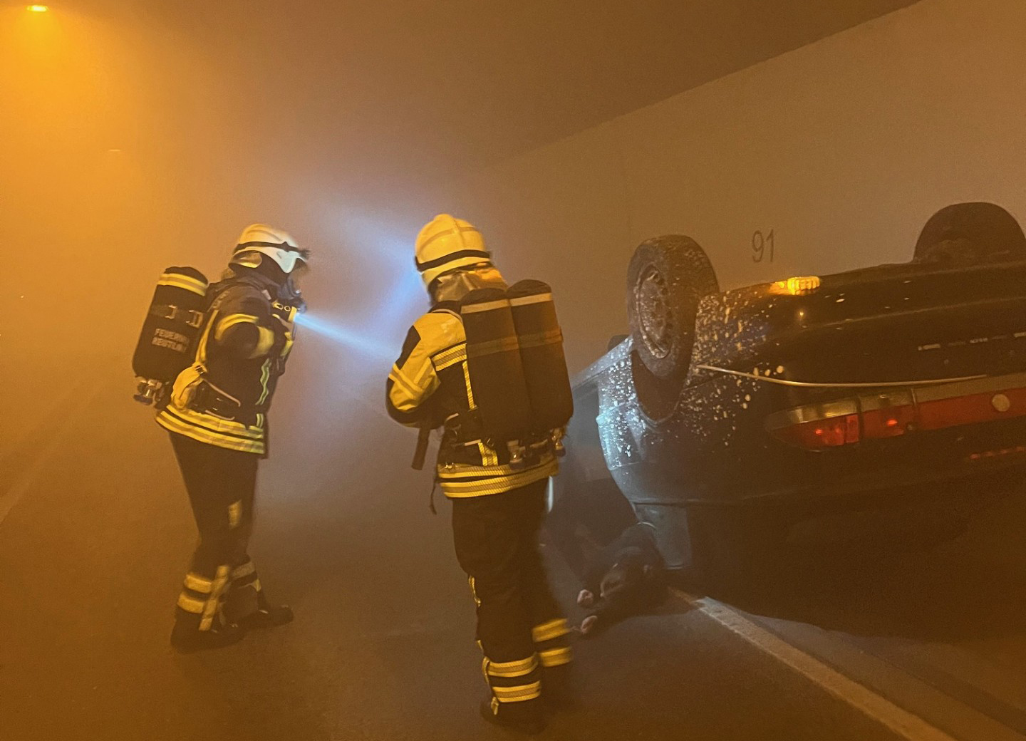 Das Bid zeigt einen Verkehrsunfall in einem Tunnel mit zwie Feuerwehrmänner bei der Beurteilung der Lage.