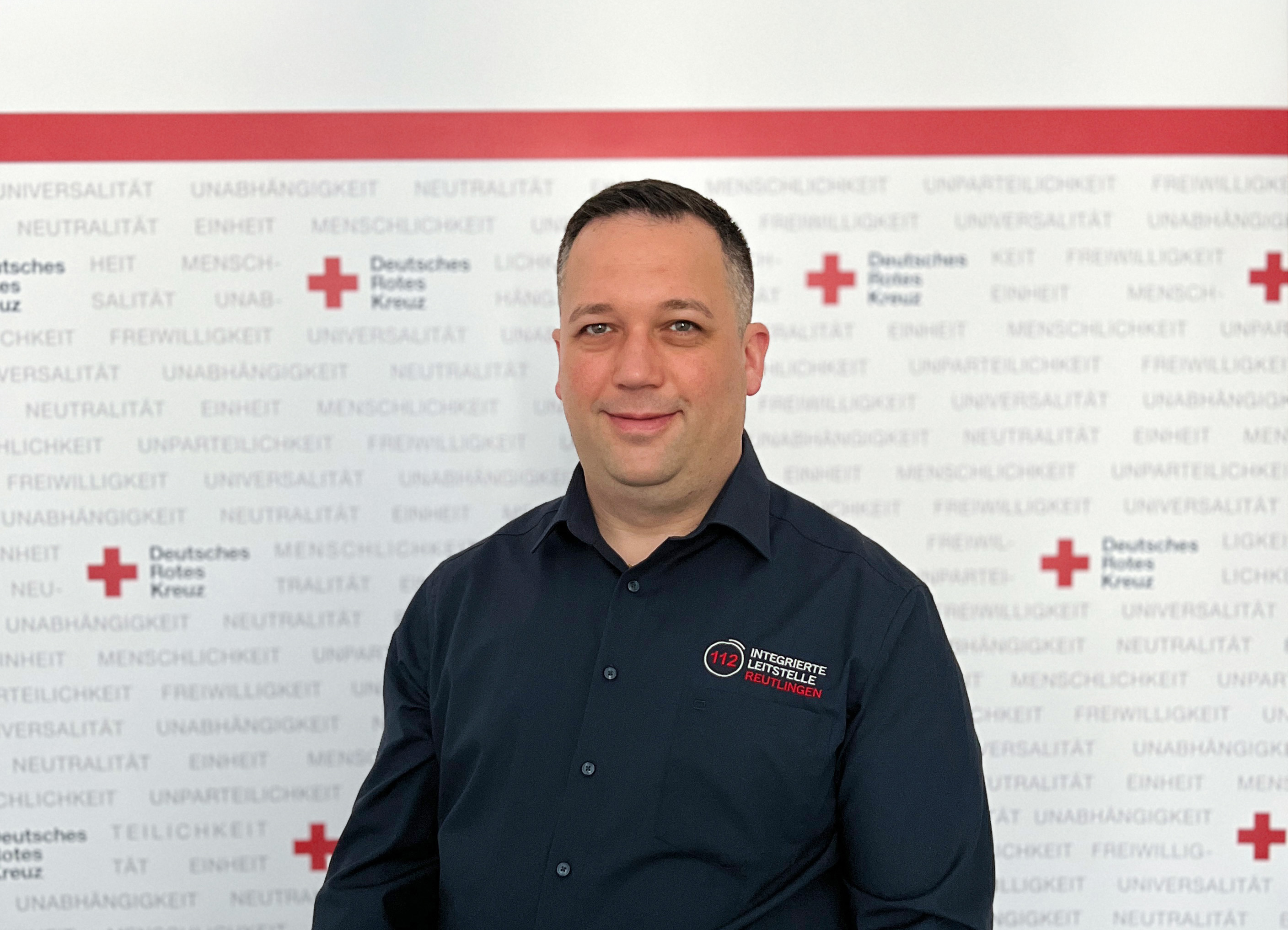 Das Bild zeigt Daniel Thüringer vor einem Banner des DRK-Kreisverbandes Reutlingen