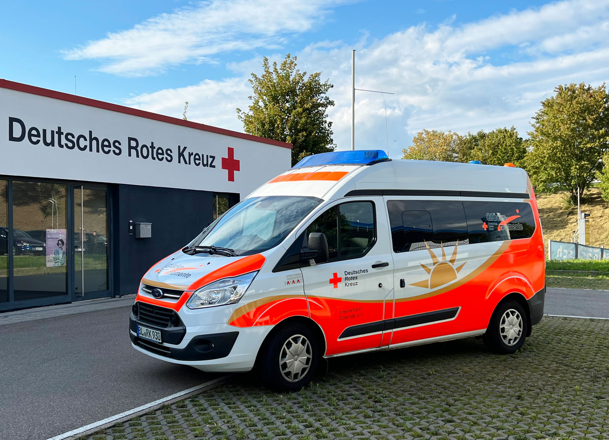 Bild: Das Glücksmomente-Fahrzeug steht vor einem DRK Gebäude. übergeben den Spendenscheck an  DRK-Kreisgeschäftsführer Thomas Födisch