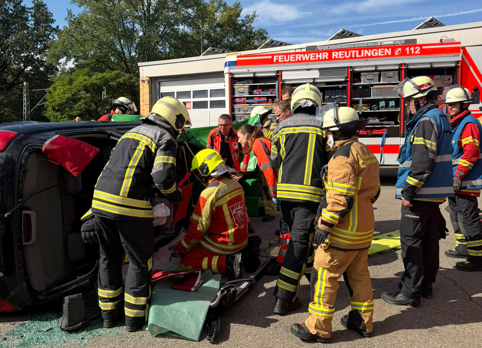Bild: Einsatzkräfte stehen vor einem Fahrzeug mit einer eingeklemmten Person. 