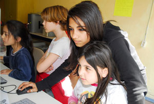 Ausländisches Mädchen zeigt jüngeren Kinden den Umgang mit dem Computer
